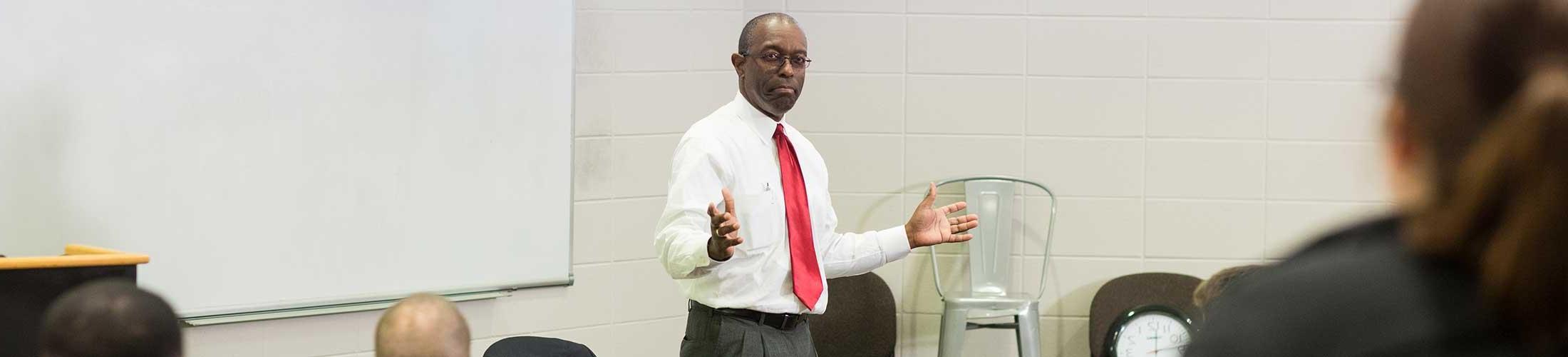 Dr. Williams in class speaking in front of board.